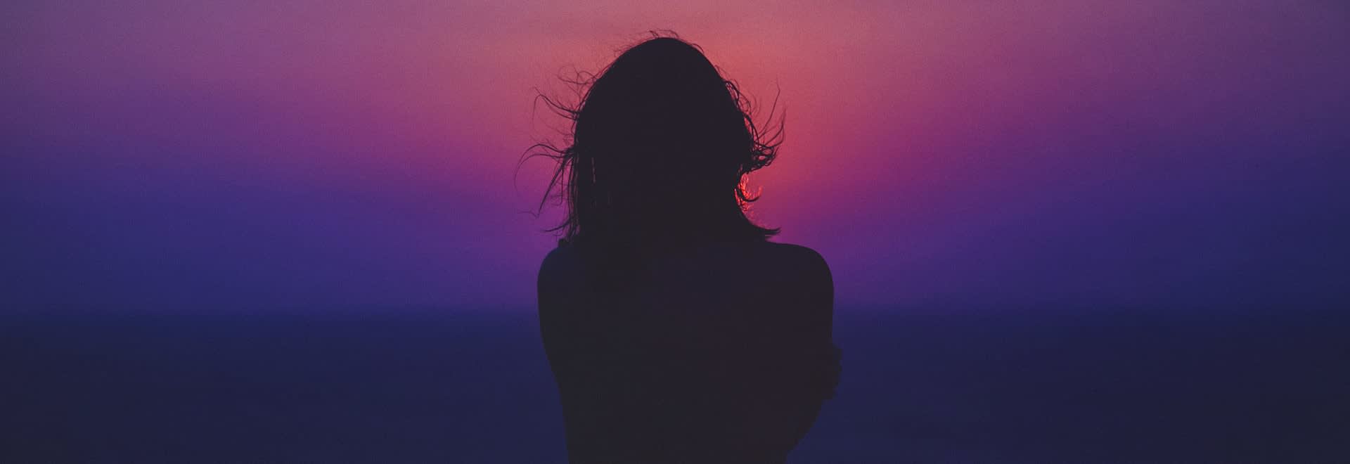 Picture of a woman facing towards colorful sunrise