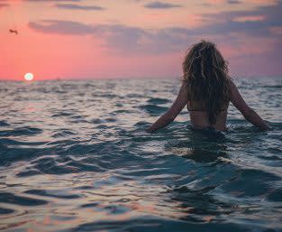 Picture of a woman with blond curly hair standing in the ocean during sunset