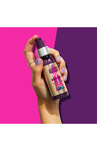 An image of Aussie 1 InHand Humidity bottle holded in hand on the pinky-purple background