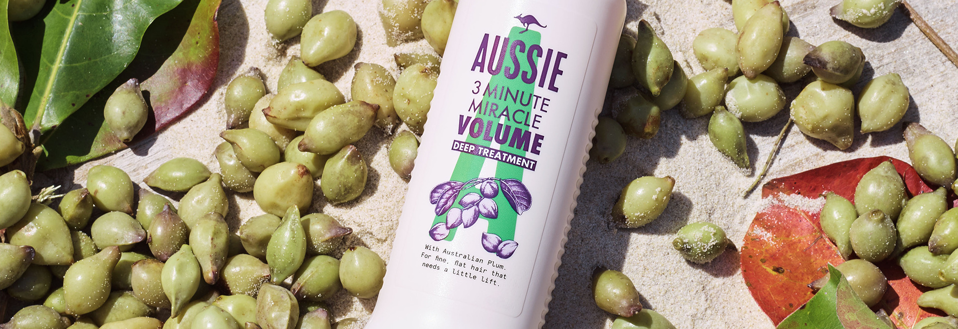 An Aussie Shampoo bottle surrounded by kakadu plums on the sand 