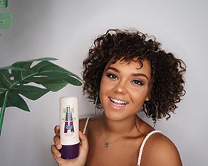 Picture of a woman with very curly hair holding conditioner bottle